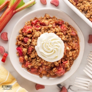 rhubarb crisp in a white bowl, topped with a swirl of whipped cream.