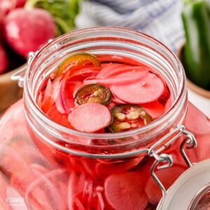 swing top glass jar filled to the top with sliced radishes in a brine.