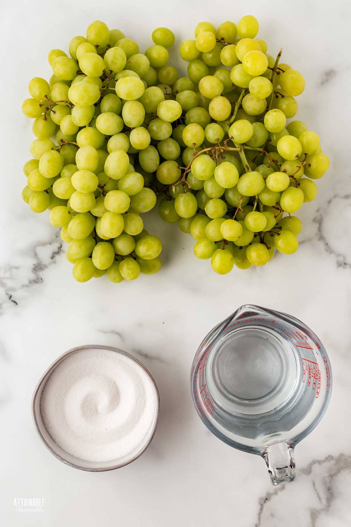 bunches of green grapes, a container of sugar, and a measuring cup of water, from above. 