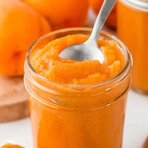 open jar of apricot preserves with a spoon in it.