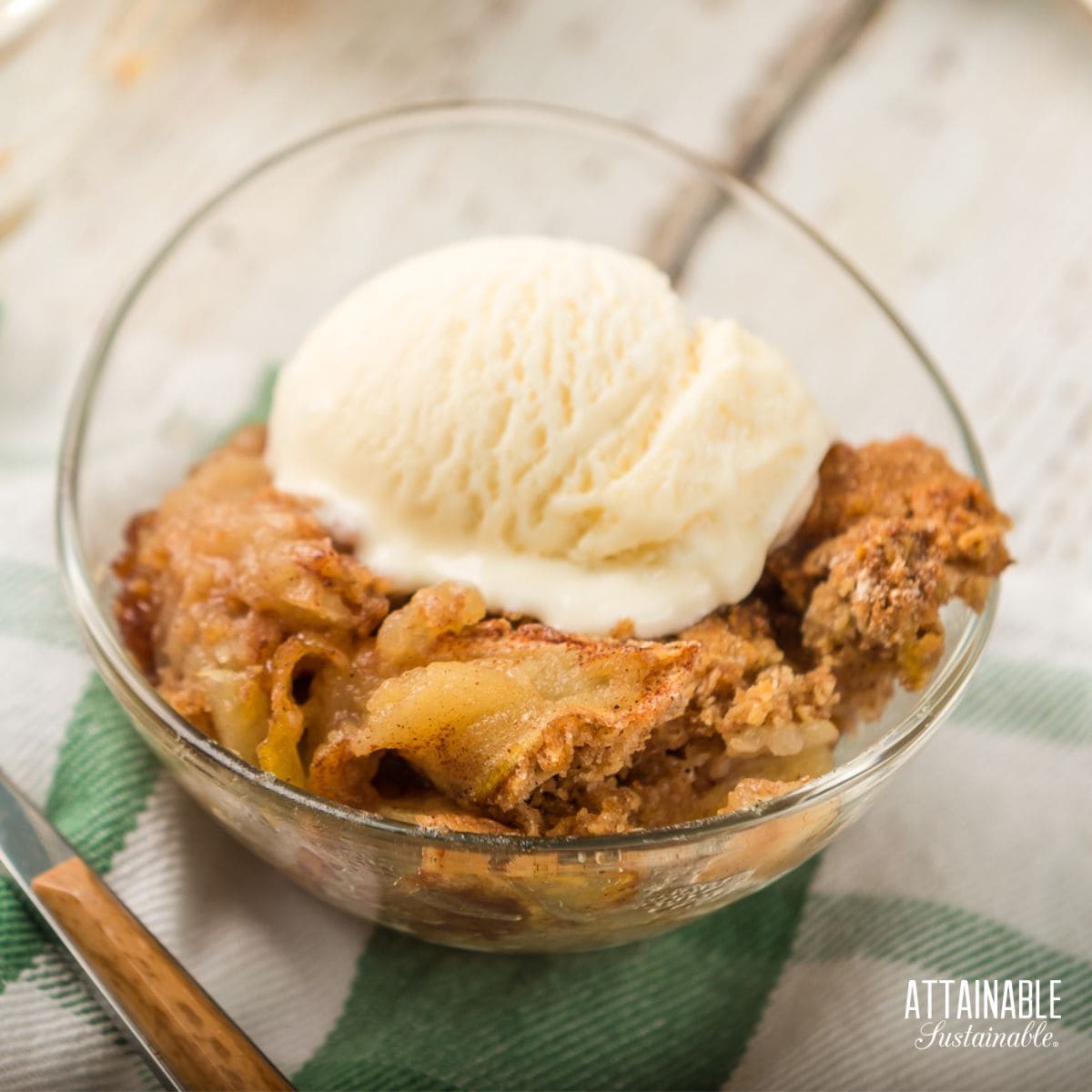 apple cobbler in a glass bowl with a scoop of ice cream.