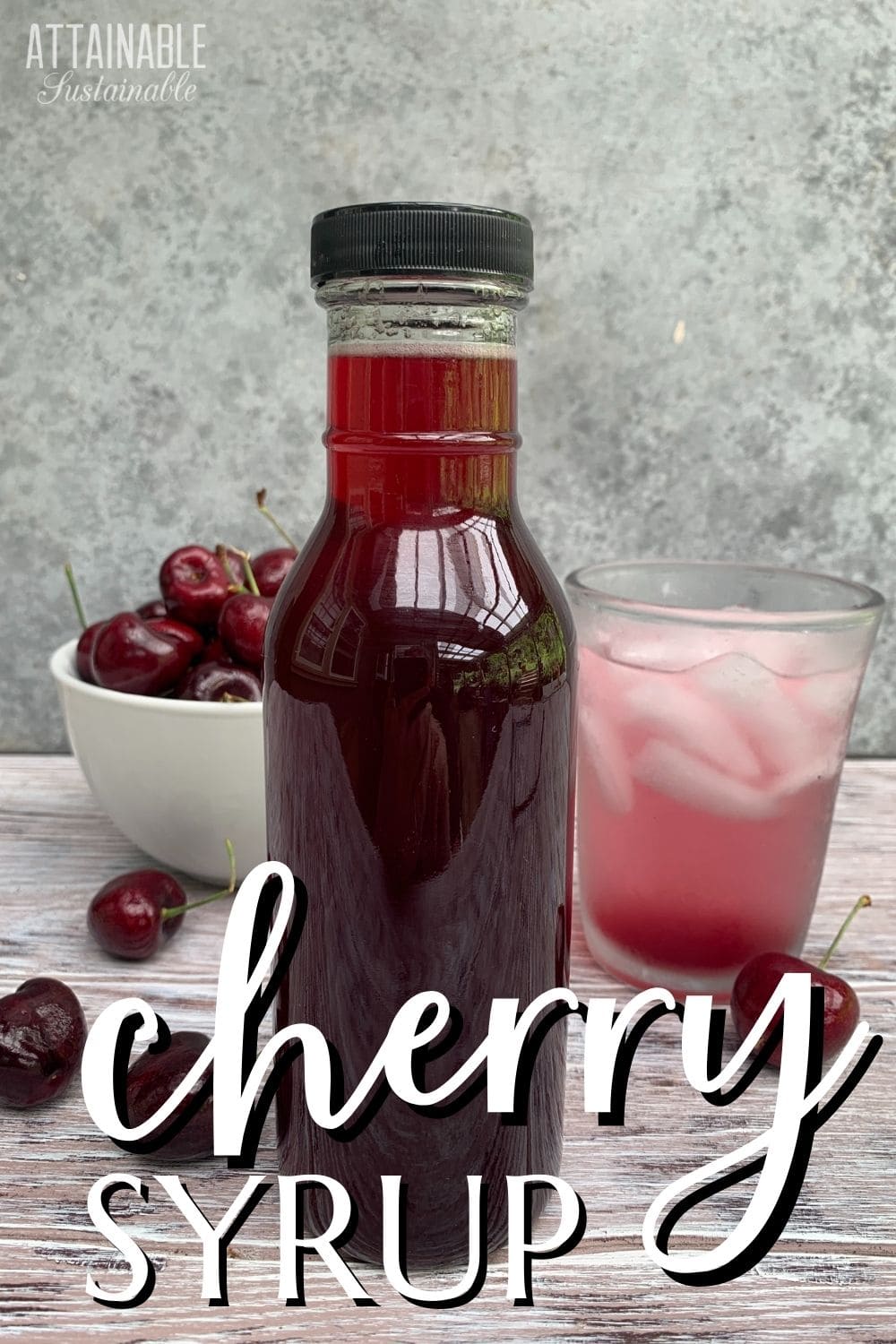 bottle of dark red cherry syrup with a bowl of cherries and an ice cold pink drink in the background.