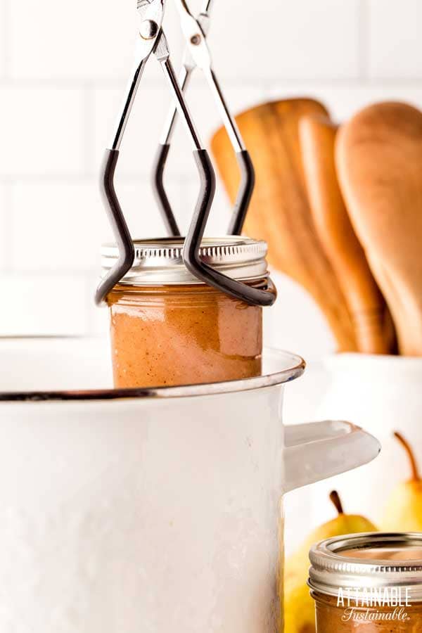 jar tongs lifting a jar of pear butter out of the canning pot.