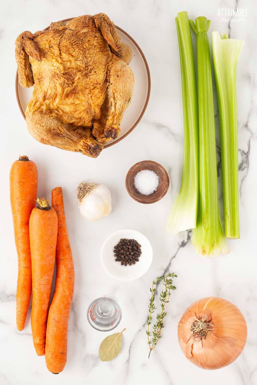 ingredients for chicken broth on a marble background: roasted chicken, onion, celery, thyme, bay leaf, garlic, carrots.