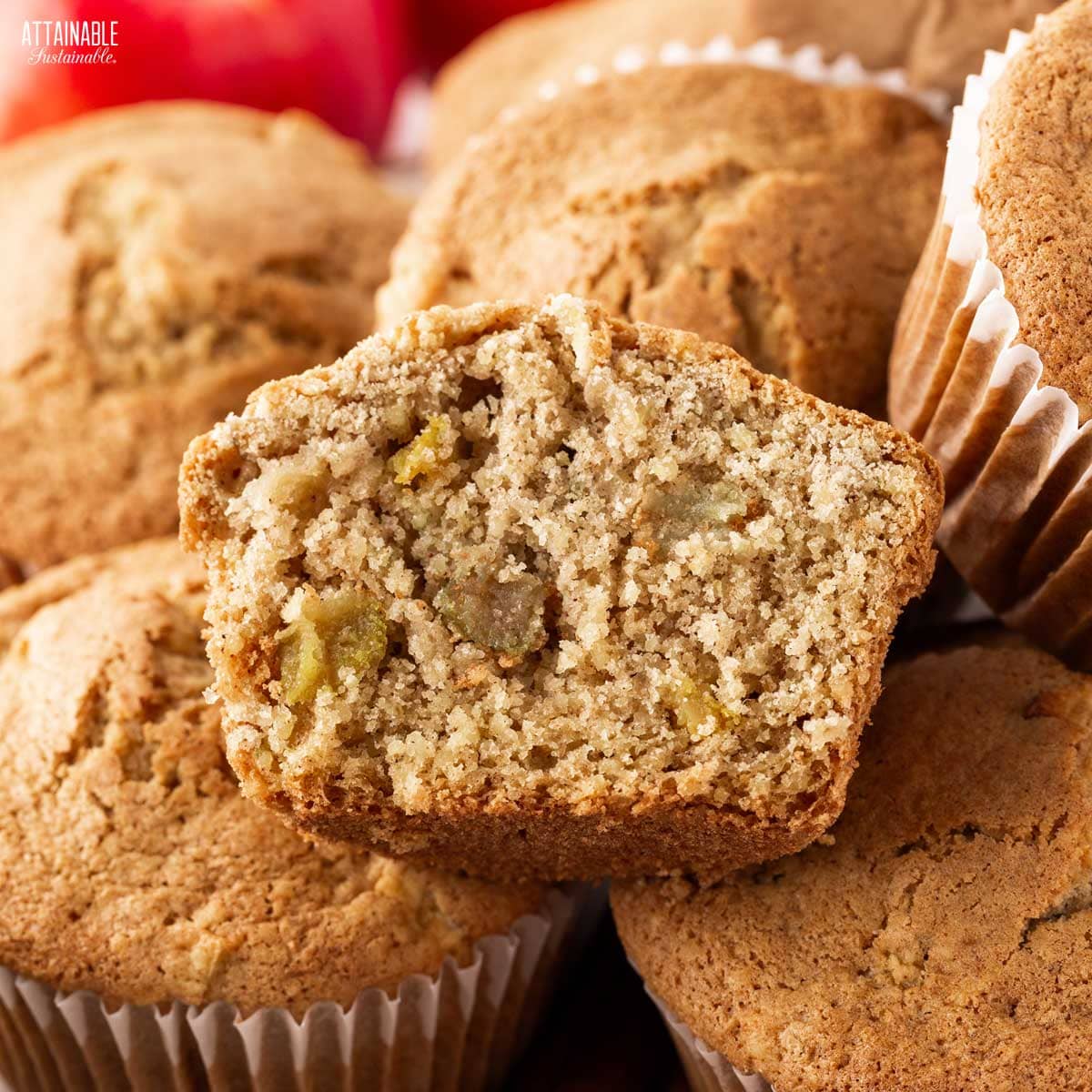 cooked apple muffin cut in half, with whole muffins underneath it.