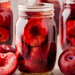 close up of glass jar full of purple canned plums.