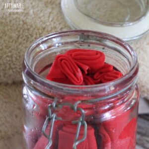 homemade dryer sheets (pink) in a glass jar with a tan towel behind.