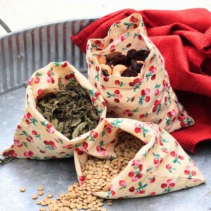 three small cloth bags (yellow fabric with red cherries) filled with dry bulk items.