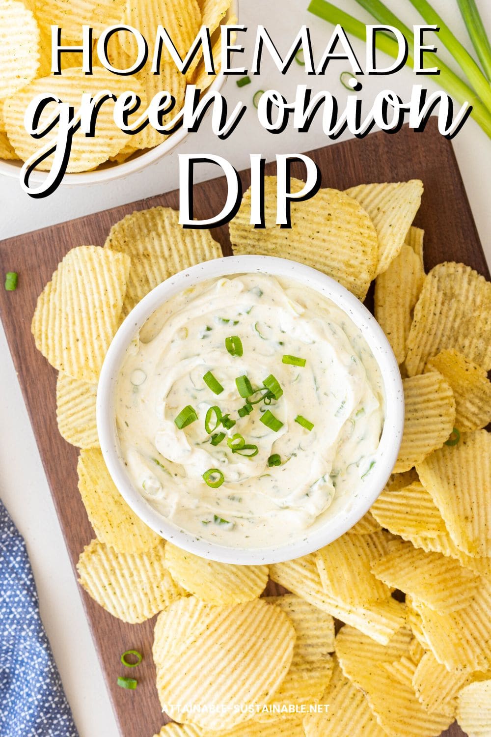 bowl of green onion dip amid potato chips on a wooden tray, from above.