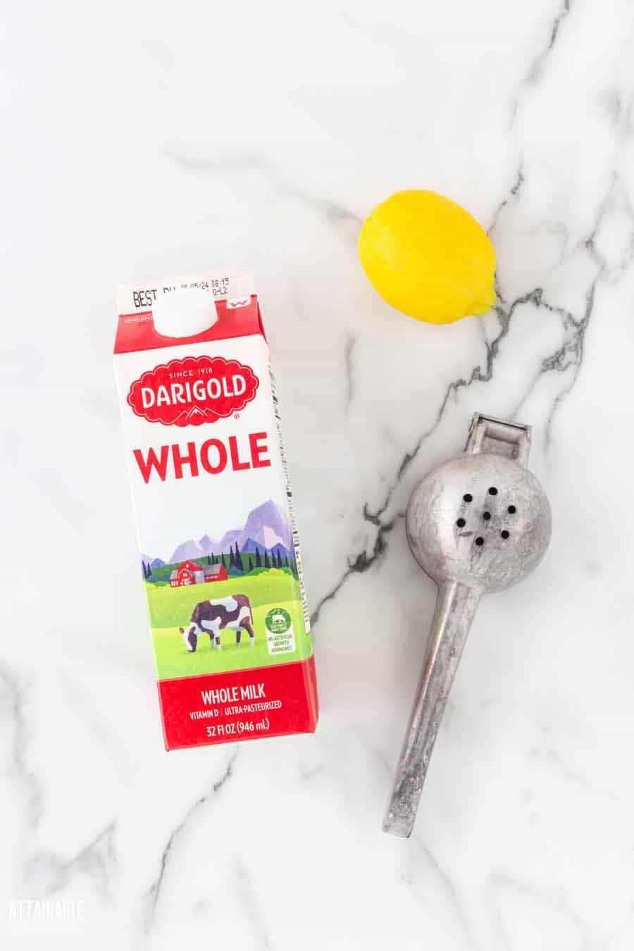 a carton of milk on a marble countertop with a lemon and a citrus juicer, from above.