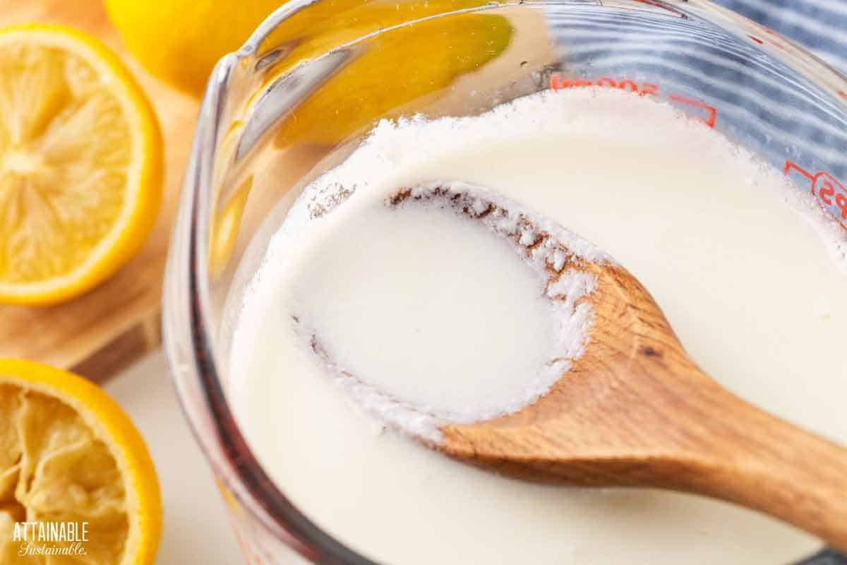 wooden spoon in a measuring cup full of soured milk, lemons in background.