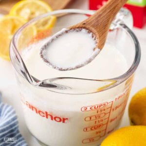 wooden spoon full of sour milk hovering above a measuring cup full of white liquid.