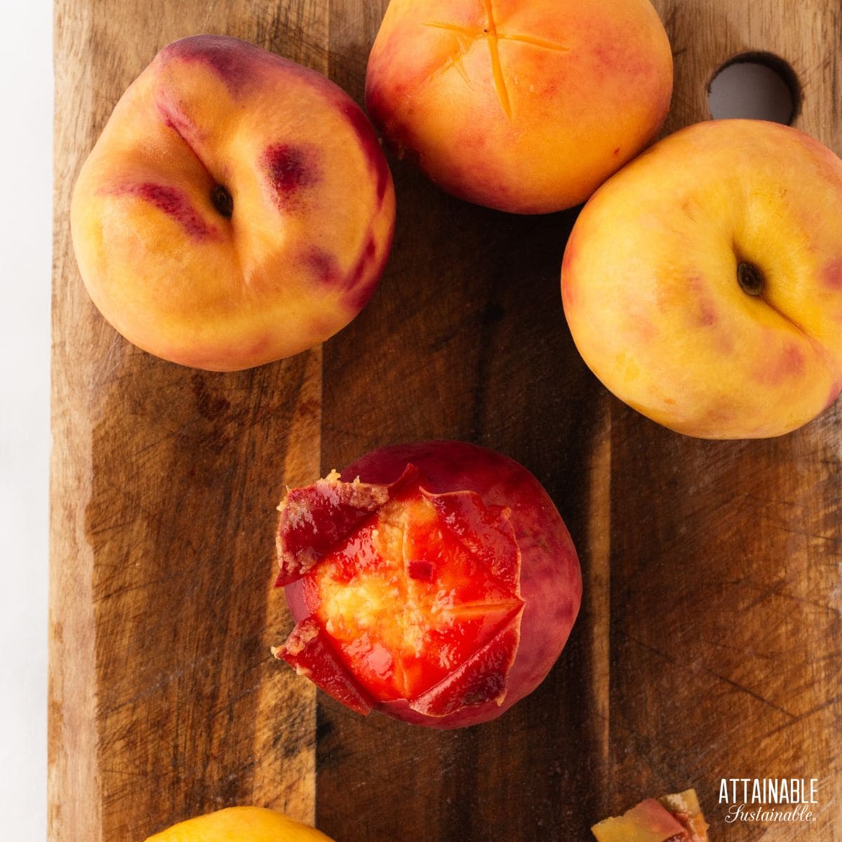 peaches in the process of being peeled, sitting on a wood cutting board.