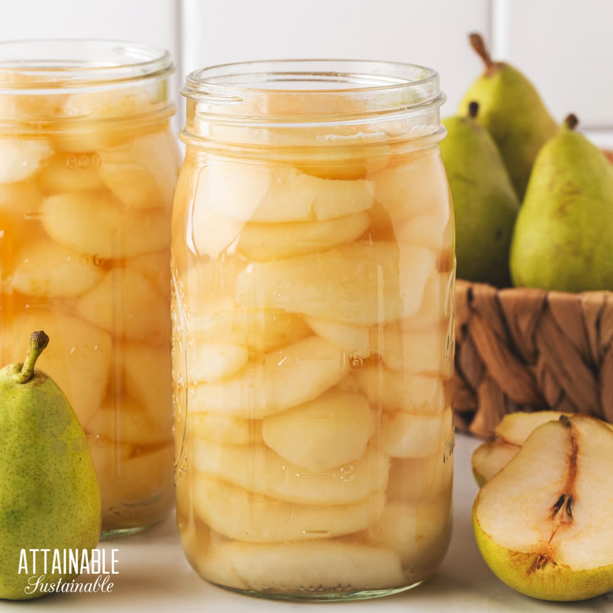 two canning jars full of pear quarters, with lids off, and green pears in a basket behind.